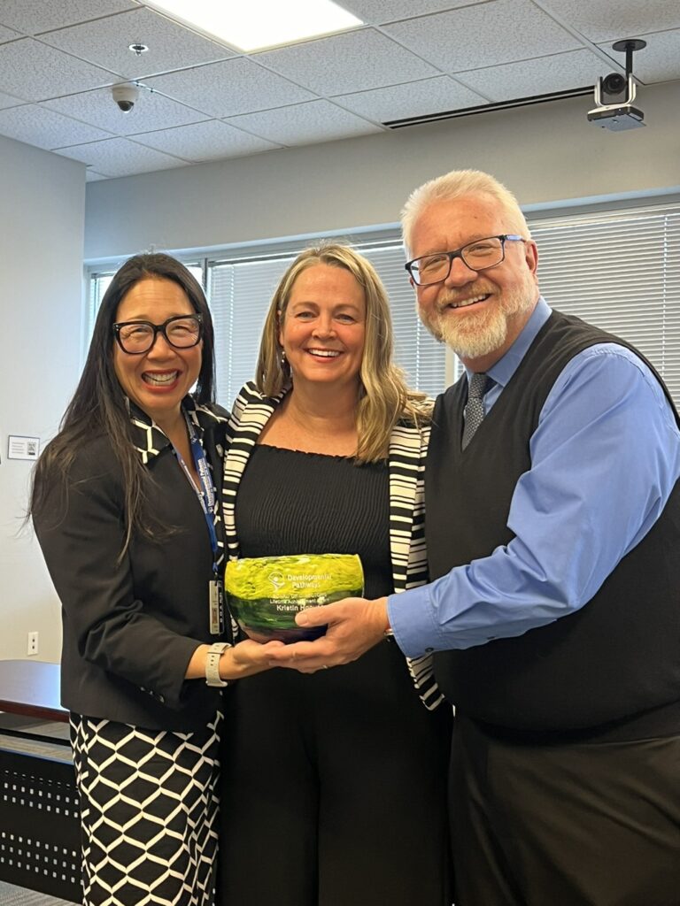 Kristin Hoover (outgoing DP board member), Jenn Conrad (DP Board President), and Matt VanAuken (CEO and Executive Director of DP) posing for the camera and holding the 2024 Developmental Pathways Board of Directors Lifetime Achievement Award.
