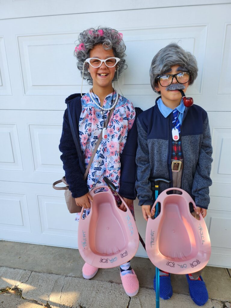 Two children dressed as elderly people, with wigs and outdated clothing. They are golding canes and bed pans.