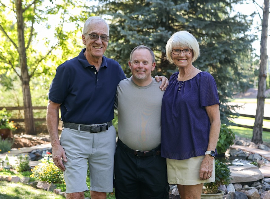 Elderly couple with their arms around their adult son smiling