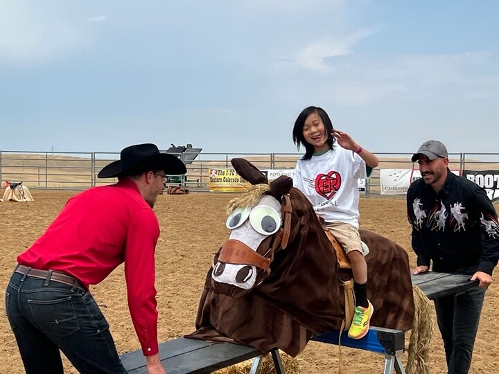 Boy riding a fake horse with 2 men helping him