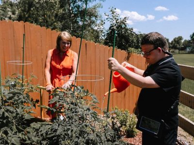 Adult boy watering plants with his mother in the garden